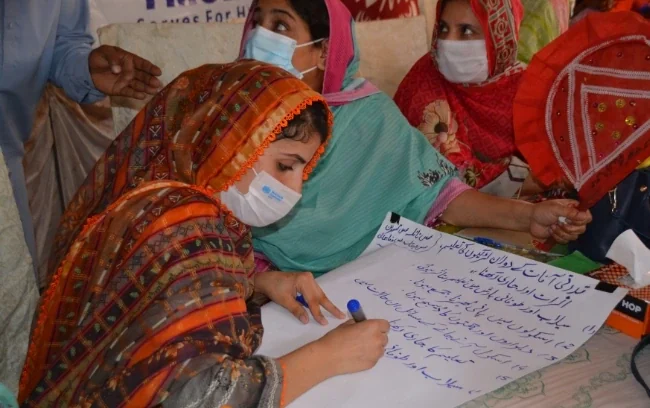 Women at a community workshop writing on chart paper.