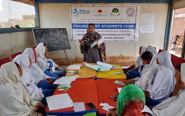 Girls seated around a table at a students' club training session.