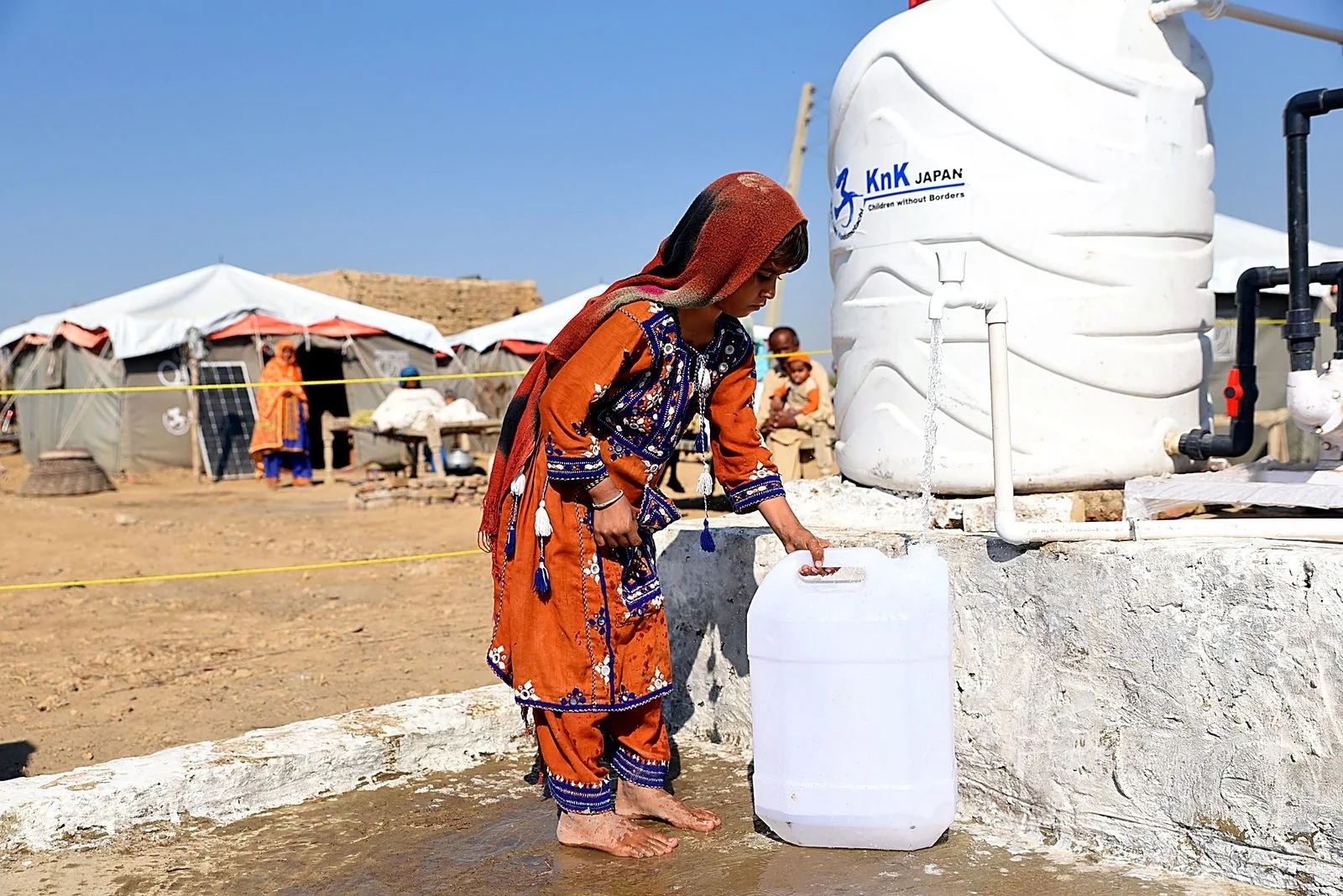 A girl fills a container from a KnK Japan water tank at a flood-response camp.