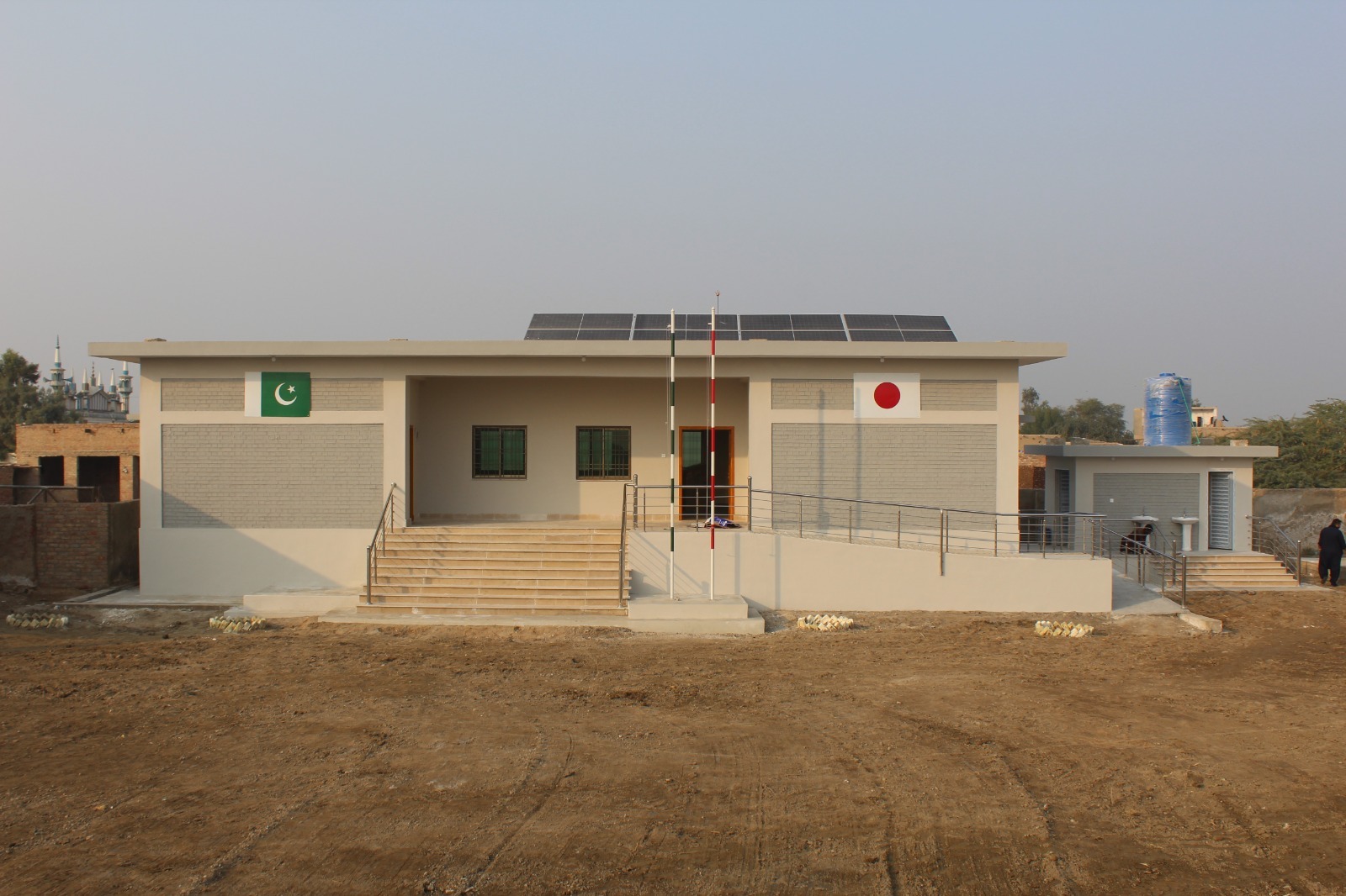 Daytime view of a newly built Basic Health Unit with solar panels, Pakistan and Japan flags