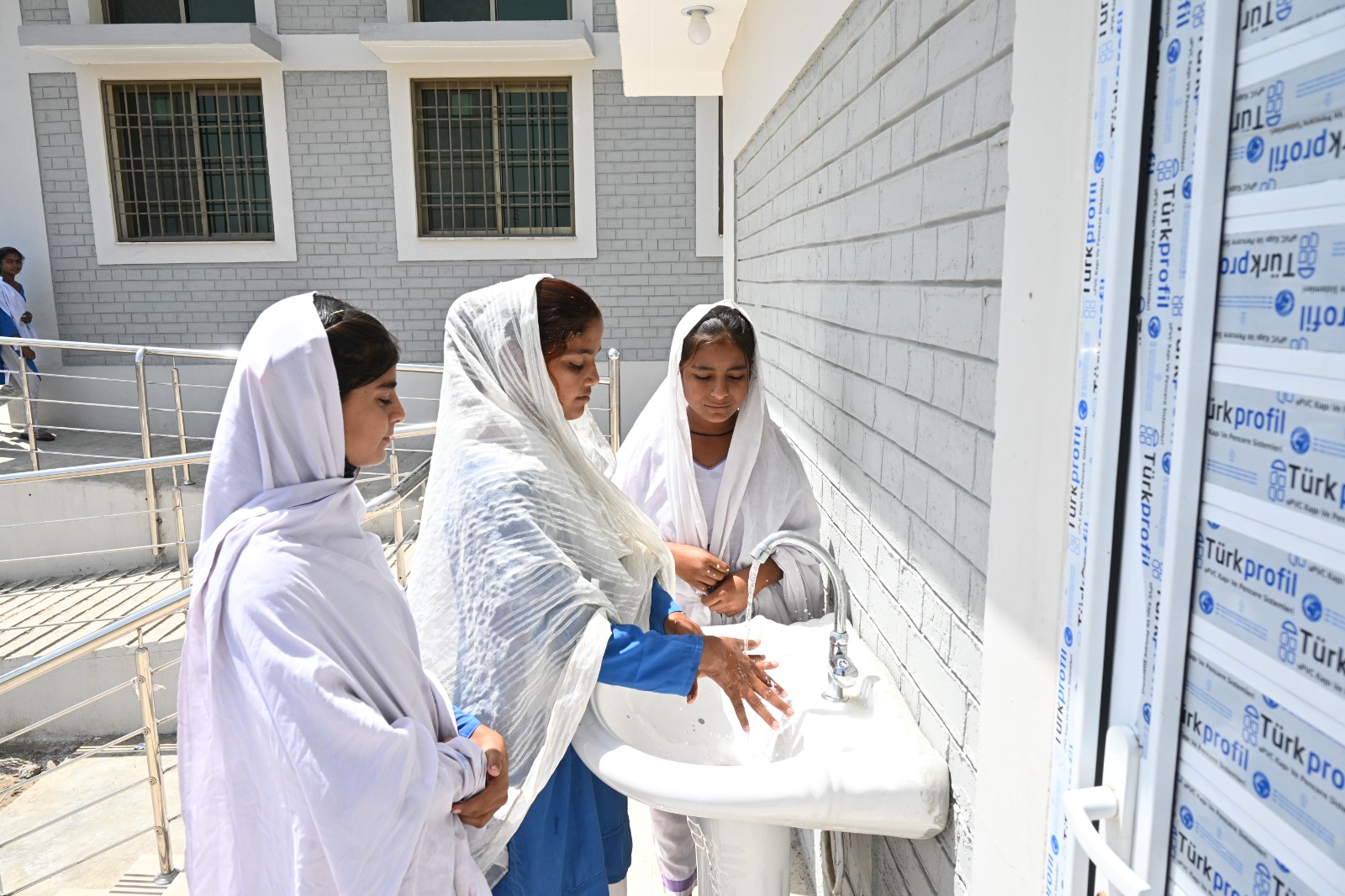 Girls washing hands at an outdoor handwashing station beside a new school building