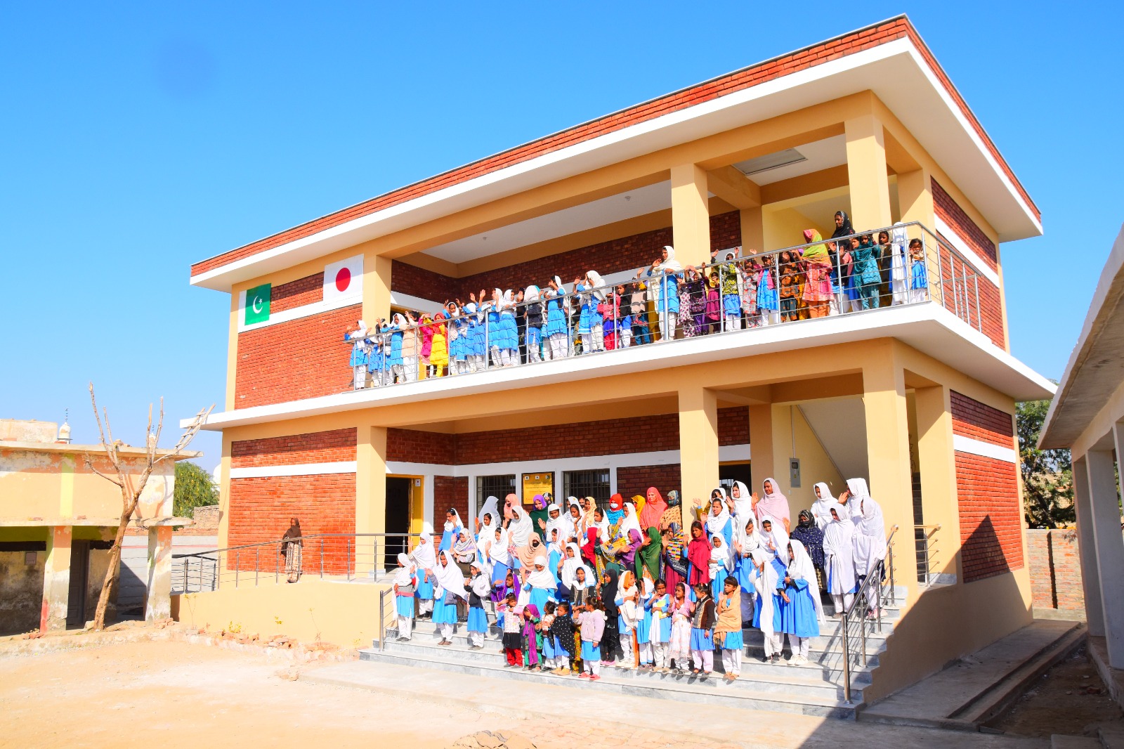 Students waving from the upper balcony of a two-storey red-brick KnK Japan school