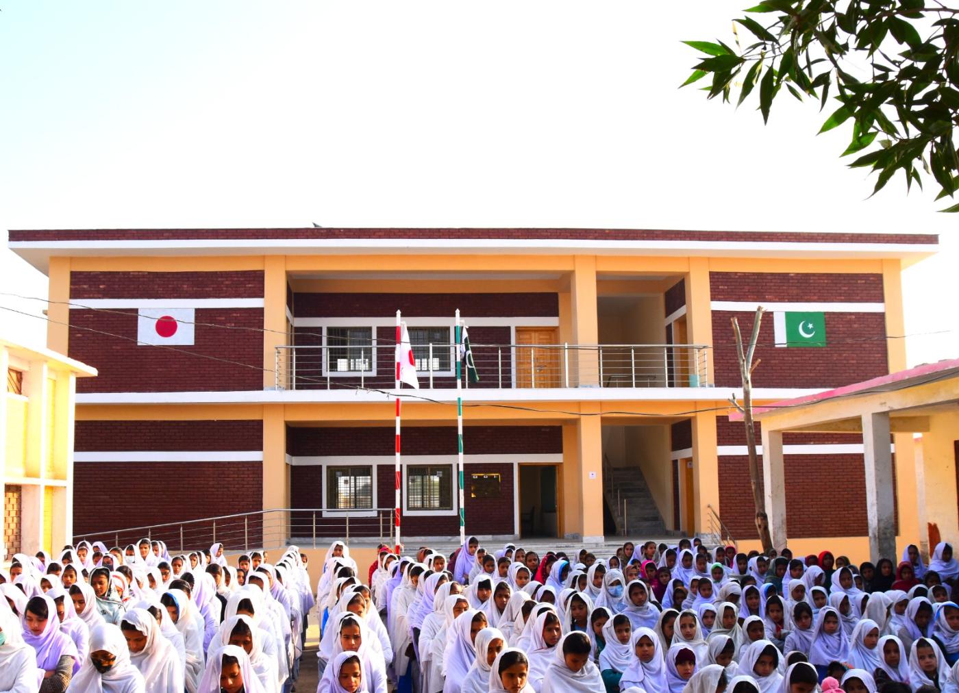 Hundreds of girls in white at morning assembly in front of a newly opened two-storey KnK Japan school in Pakistan